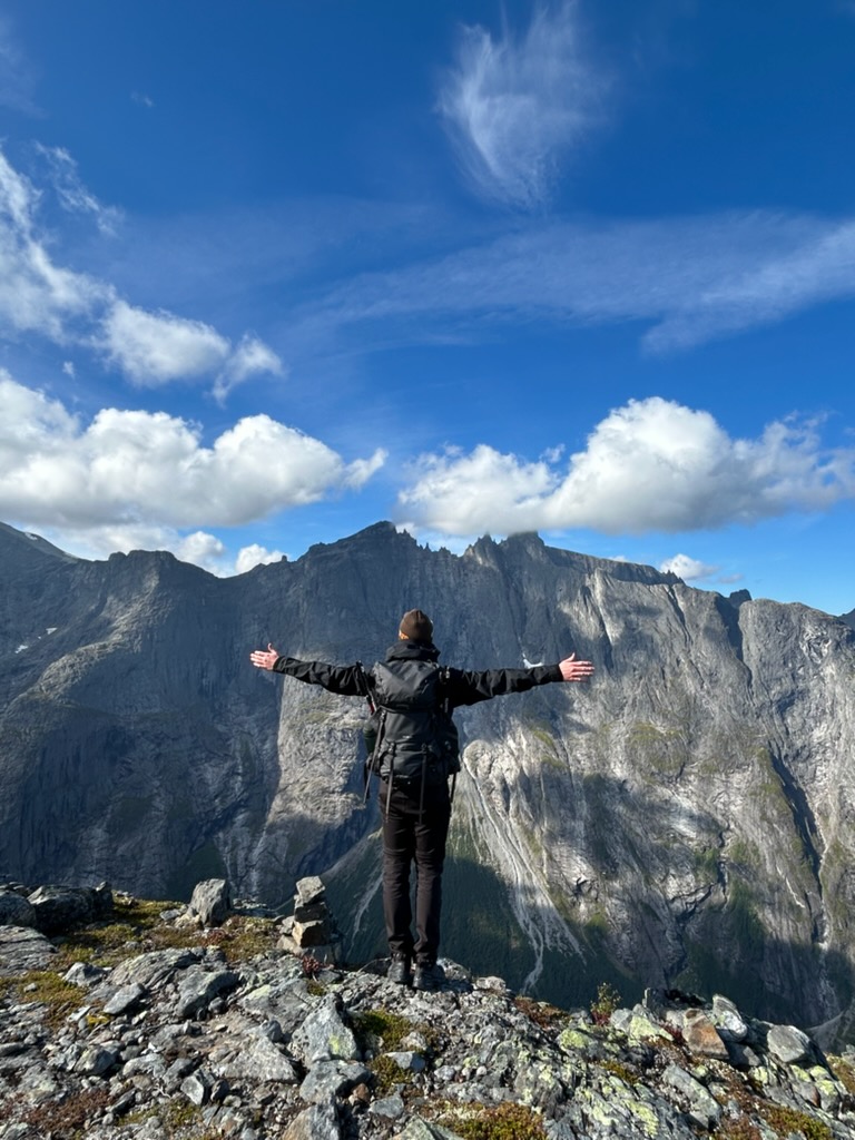 En person står med utsträckta armar på en bergstopp i Norge
